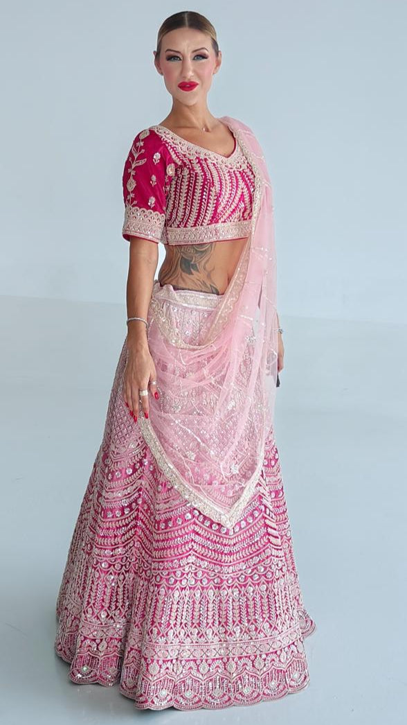 Woman wearing a pink traditional outfit with intricate designs on a light gray background